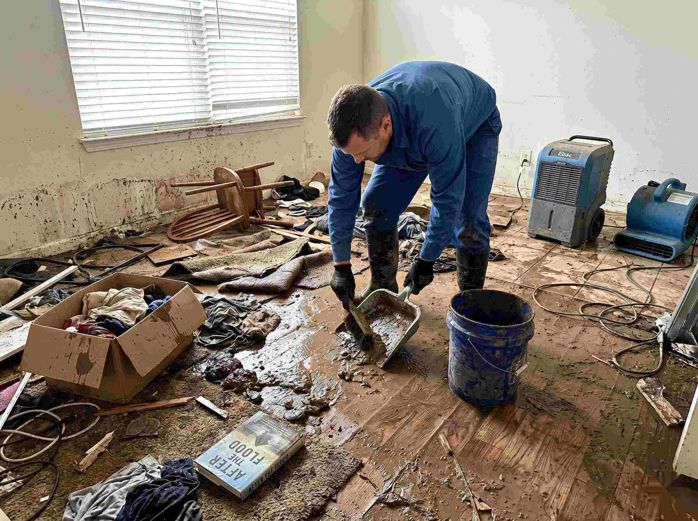 Realistic photo of a technician performing mud and debris removal after a home flood in Ann Arbor, showing soaked furniture, wet flooring, and scattered debris during post-flood cleanup.