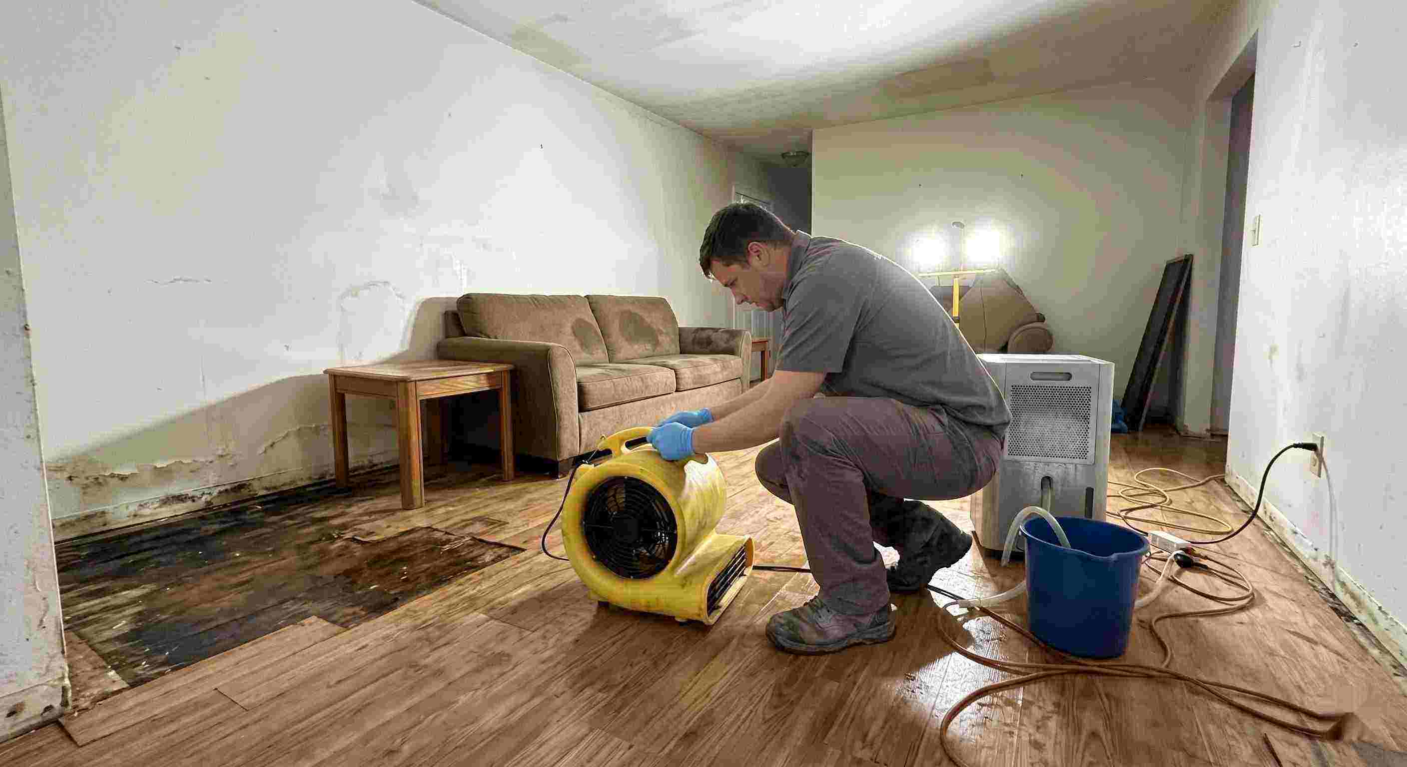 Professional water damage restoration technician drying wet floors with equipment during cleanup process in Flint